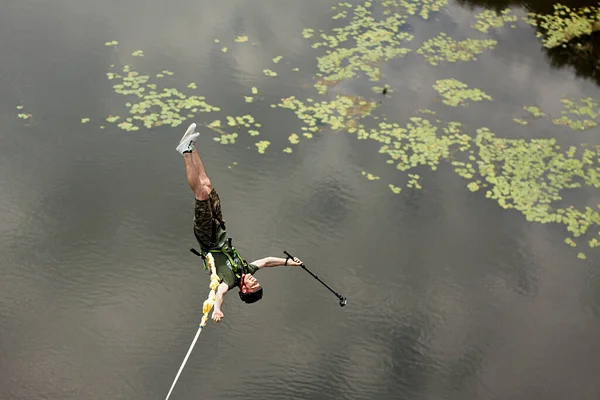 Concept of Extreme Sports and Fun. A man is a  thrill-seeker and a  rope jumper from the bridge. He is very happy to make a dream come true. He  is holding an action camera and insanely happy