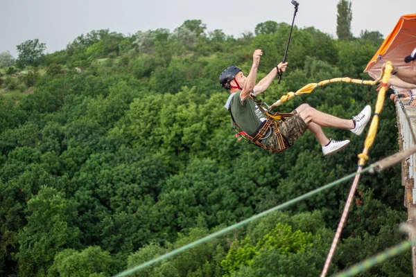 Concept of Extreme Sports and Fun. The man is a  thrill-seeker and a  rope jumper from the bridge. He is very happy to make a dream come true. He  is holding an action camera and insanely happy