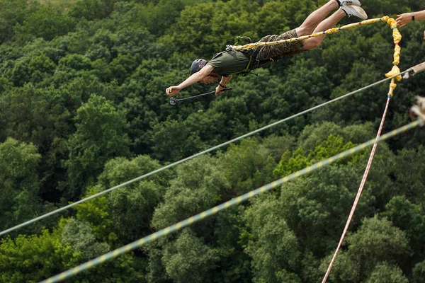 Concept of Extreme Sports and Fun. A man is a  thrill-seeker and a  rope jumper from the bridge. He is very happy to make a dream come true. He  is holding an action camera and insanely happy