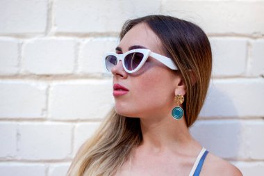 Bir kadın dışarıda beyaz tuğla duvarın yanında duruyor.