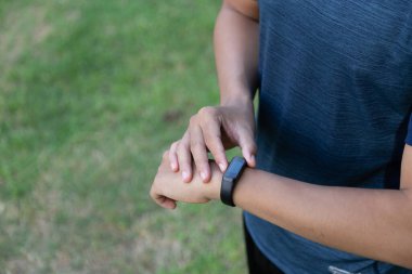 Asyalı genç fitness koşucusu akıllı saat bandını kontrol ediyor.