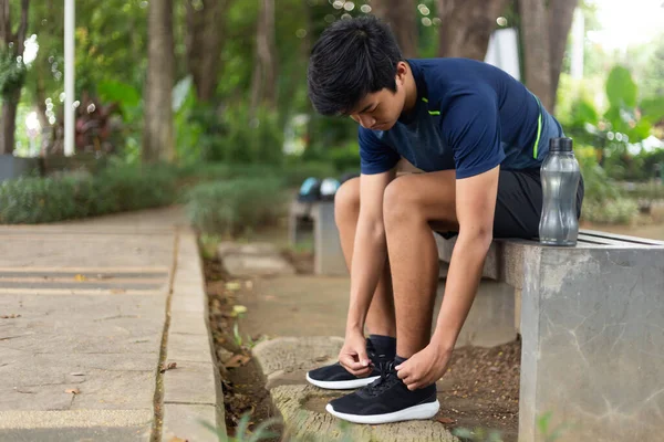Asyalı genç fitness koşucusu sandalyeye otur ve koşu ayakkabılarını bağla.