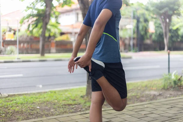 Asyalı genç fitness koşucusu parkta koşmadan önce bacağını çırpıyor.