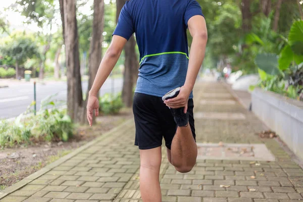 asian young fitness man runner do a strething leg before running at the park