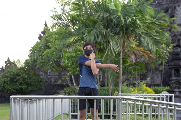 Asyalı genç fitness koşucusu parkta koşmadan önce ısınıyor.