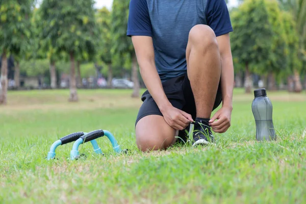 Asyalı genç fitness koşucusu parkta koşu ayakkabısı bağlıyor.
