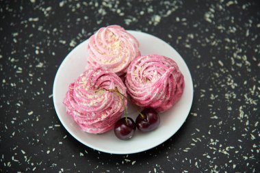 Pembe şekerlemelere yakın beyaz bir tabakta tatlı kirazlar.