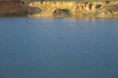 Altın saatinde suyun yüzeyindeki yüksek sarp kıyılar. Doğal mavi arkaplan ve sarı şerit.