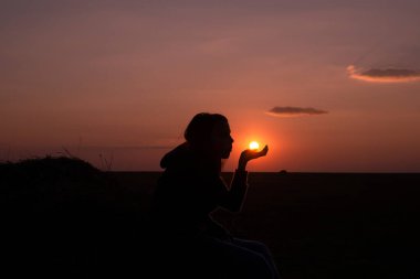 Gün batımında oturan, elinde güneşi tutan ve üfleyen bir kızın silueti. Mistisizm ve büyü kavramı