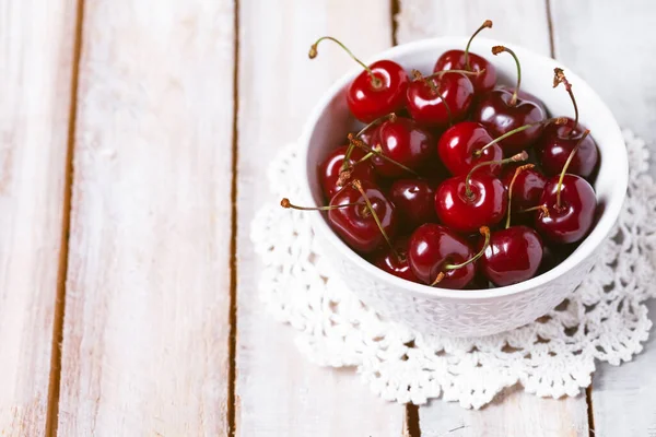 Sweet ripe red cherry in white bowl on vintage napkin. Summer natural low calories dessert. Wooden background. Close up macro. Copy space for text