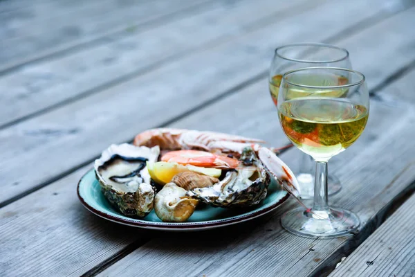 Delicious romantic gourmet lunch for two. Fresh raw oysters, shrimps, snails with glass of cold white wine. Perfect gormand lunch, traditional french appetizer. Wooden background, close up