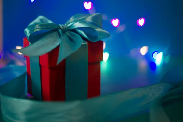 Rote Geschenkschachtel mit blauem Band auf blauem Hintergrund mit farbigen Lichtern — Stockfoto