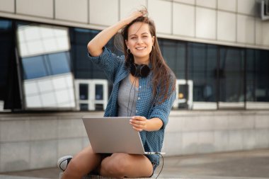 Genç ve güzel bir kız laptopun başına oturur ve korkulukta oturup müzik dinler.