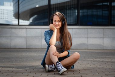 Genç ve güzel bir kız laptopun başına oturur ve korkulukta oturup müzik dinler.