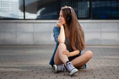 Genç ve güzel bir kız laptopun başına oturur ve korkulukta oturup müzik dinler.