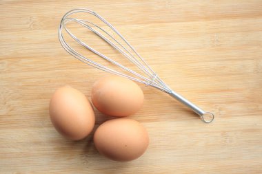 Çırpma teli ve ahşap arka plan üzerinde yumurta