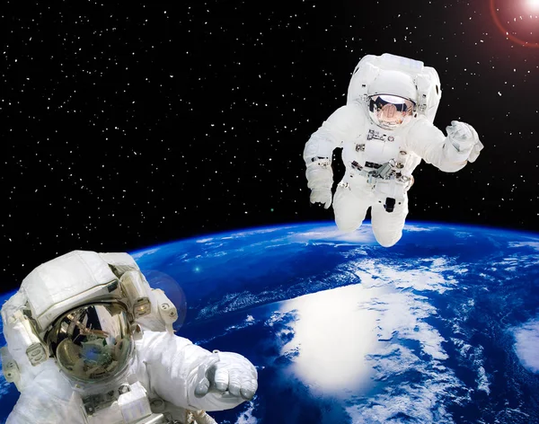 Earth and astronauts in space suits in outer space. Space walk.