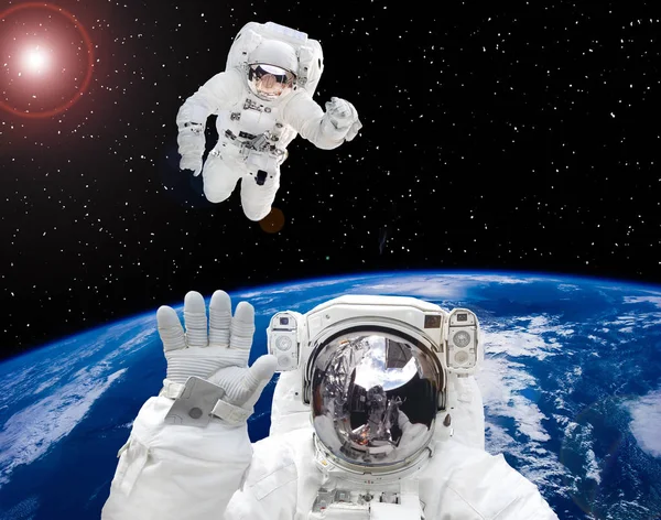 Earth and astronauts in space suits in outer space. Space walk.