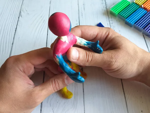 The hands of a male craftsman work on a human sculpture, sculpting from plasticine against the background of a table top made of white boards. The view from the top. Concept of a hobby or workflow.