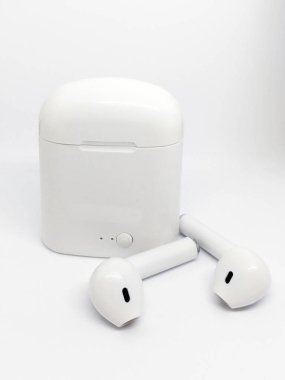 Beyaz kablosuz kulaklık ve beyaz bir arka planda şarj çantası. Şarj çantasının yanında bir çift modern kablosuz kulaklık duruyor. Metin ve logo için yer.