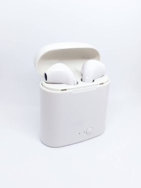 Beyaz kablosuz kulaklık ve beyaz bir arka planda şarj çantası. Şarj kutusunun içinde bir çift modern kablosuz kulaklık. Metin ve logo için boşluk.