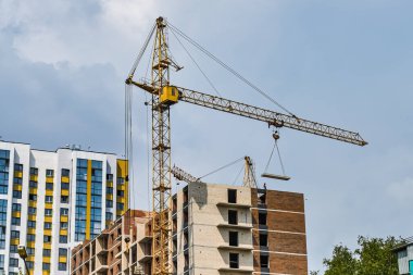 Çok katlı bir binanın inşaatı, bir vinç beton levhayı yeni inşa edilmiş bir binanın arka planına kaldırıyor. Şehir içinde şehir içi gelişim. İnşaat alanında ereksiyon vinci.