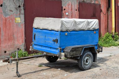 Arabalar için kargo karavanı. Metal kapılı beton bir duvarın arka planında eski bir araba römorku var. Nakliye masrafları için karavan ayrı..