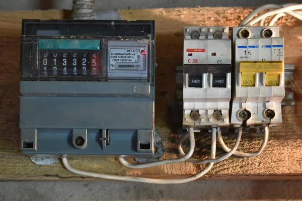 Old electricity meter and circuit breaker on a wooden substrate inside an old room under artificial lighting. Electrical safety in homes, with circuit breakers and energy meter. Home electrical system