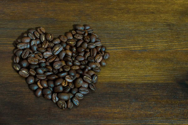 Heart shaped coffee beans on brown wooden background. Top view or macro of heart shaped fresh organic roasted coffee beans on wooden surface. Lovely coffee beans with wooden table.  Place for text