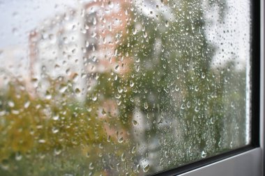 Yağmurlu bir günde pencere camında yağmur damlaları. Yağmur damlalarıyla kaplı camların arasından sonbahar bulutlu havası. Bulanık sonbahar şehri. Yağmur damlalarına seçici odaklanma.