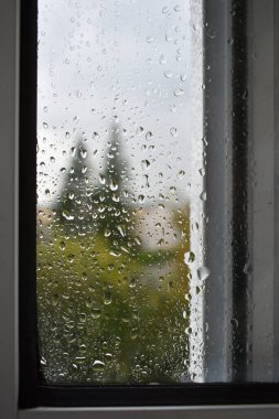 Yağmurlu bir günde pencere camında yağmur damlaları. Yağmur damlalarıyla kaplı camların arasından sonbahar bulutlu havası. Bulanık sonbahar şehri. Yağmur damlalarına seçici odaklanma.