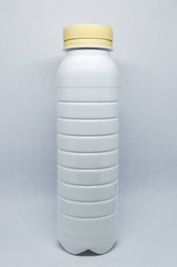 Gri arka planda bej kapaklı beyaz plastik şişe. Sıvılar ve süt ürünleri için boş plastik şişe. Plastik şişe şablonu. Ekolojik sorunlar: Plastiğin geri dönüşümü.