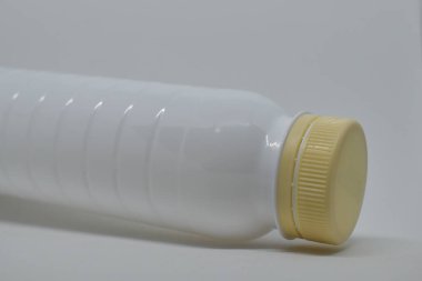 Gri arka planda bej kapaklı beyaz plastik şişe. Sıvılar ve süt ürünleri için boş plastik şişe. Plastik şişe şablonu. Ekolojik sorunlar: Plastiğin geri dönüşümü.
