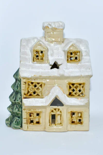 Ceramic decor: a Christmas toy house with a Christmas tree on a white background. Vintage decorative candlestick in the form of a house with a snow-covered roof. Isolated on white. New Year decoration