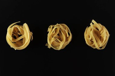İtalyan makarnası çeşitleri, pişmemiş çiğ makarna ve siyah arka planda izole edilmiş tagliatelle..