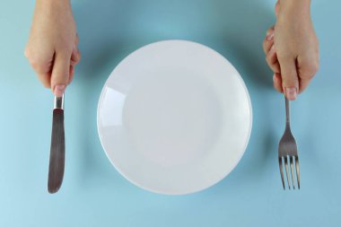 Çatalı, bıçağı ve mavi arka planda boş tabağı olan bir kadın.