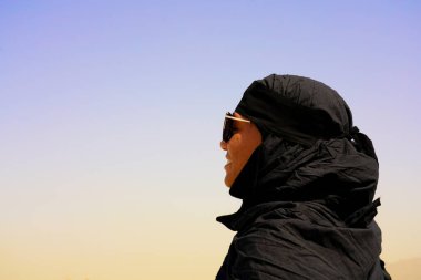 Siyah abaya 'da kreal mavi gökyüzü ile güneş gözlüklü güzel bir genç kadın portresi.