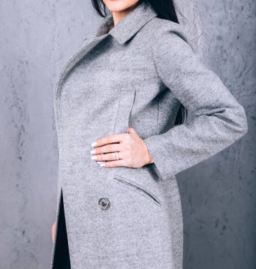 Dış giyimin ayrıntıları yakın plan. Yarı sezon kıyafetlerinin stüdyo fotoğrafçılığı. Gri arka planda zarif ceketli genç bir kız. Promosyon kadın ceketi. Şık bir sonbahar bahar montu giymiş bir kadın..