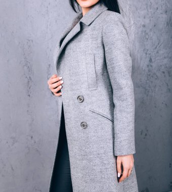 Dış giyimin ayrıntıları yakın plan. Yarı sezon kıyafetlerinin stüdyo fotoğrafçılığı. Gri arka planda zarif ceketli genç bir kız. Promosyon kadın ceketi. Şık bir sonbahar bahar montu giymiş bir kadın..