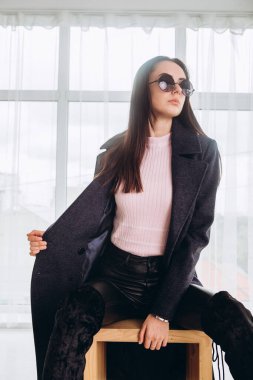 Stüdyoda ceketli bir kız sandalyede oturuyor. Açık havada zarif ceketli genç bir kız. Promosyon kadın ceketi. Havalı, yünlü bir sonbahar ve bahar ceketli, şık, esmer bir kadın..