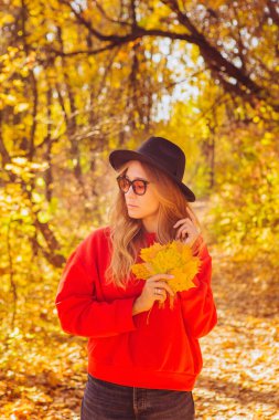Sonbahar ormanındaki bir sarışının portresi. Siyah şapkalı güzel kız parkta yürüyor. Dışarıdaki şık aksesuarlı kadın. Gün batımında doğada bir kızın portresi. sarı sonbahar arkaplanı