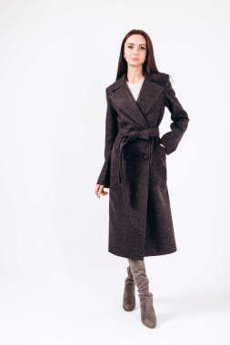 Beyaz arka planda, kalın ceketli bir kız. Dış giyim mankeni. Uzun siyah ceketli esmer. Rahat montlu güzel bir kız. Bahar sonbahar koleksiyonu. Esmer bir ceketin portresi, tam boy..