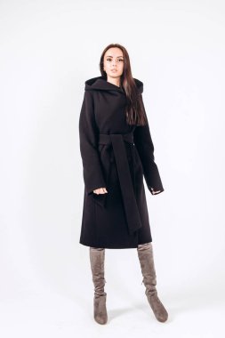 Beyaz arka planda, kalın ceketli bir kız. Dış giyim mankeni. Uzun siyah ceketli esmer. Rahat montlu güzel bir kız. Bahar sonbahar koleksiyonu. Esmer bir ceketin portresi, tam boy..