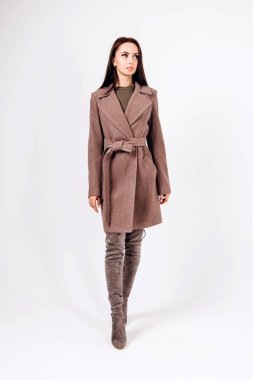 Beyaz arka planda, kalın ceketli bir kız. Dış giyim mankeni. Uzun bej ceketli esmer. Rahat montlu güzel bir kız. Bahar sonbahar koleksiyonu. Esmer bir ceketin portresi, tam boy..