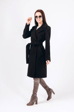 Beyaz arka planda, kalın ceketli bir kız. Dış giyim mankeni. Uzun siyah ceketli esmer. Rahat montlu güzel bir kız. Bahar sonbahar koleksiyonu. Esmer bir ceketin portresi, tam boy..