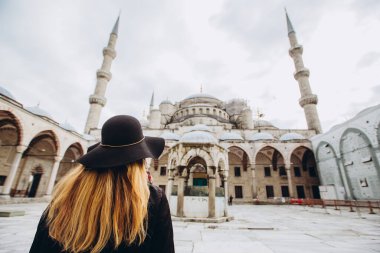 Türkiye 'nin İstanbul kentindeki mavi camiye bakan şapkalı ve siyah ceketli genç bir kadın. Bir kız kışın İstanbul 'da yürüyor. Sonbahar günü caminin arka planında gezgin bir sarışının fotoğrafı..