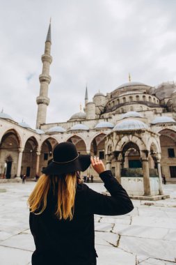 Türkiye 'nin İstanbul kentindeki mavi camiye bakan şapkalı ve siyah ceketli genç bir kadın. Bir kız kışın İstanbul 'da yürüyor. Sonbahar günü caminin arka planında gezgin bir sarışının fotoğrafı..