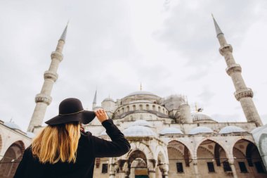 Türkiye 'nin İstanbul kentindeki mavi camiye bakan şapkalı ve siyah ceketli genç bir kadın. Bir kız kışın İstanbul 'da yürüyor. Sonbahar günü caminin arka planında gezgin bir sarışının fotoğrafı..