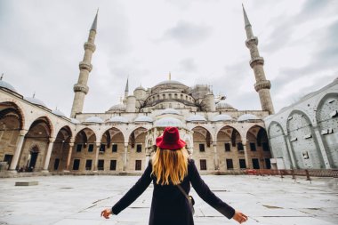 Türkiye 'nin İstanbul kentindeki mavi camiye bakan şapkalı ve siyah ceketli genç bir kadın. Bir kız kışın İstanbul 'da yürüyor. Sonbahar günü caminin arka planında gezgin bir sarışının fotoğrafı..