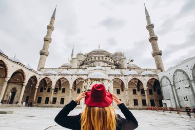 Türkiye 'nin İstanbul kentindeki mavi camiye bakan şapkalı ve siyah ceketli genç bir kadın. Bir kız kışın İstanbul 'da yürüyor. Sonbahar günü caminin arka planında gezgin bir sarışının fotoğrafı..